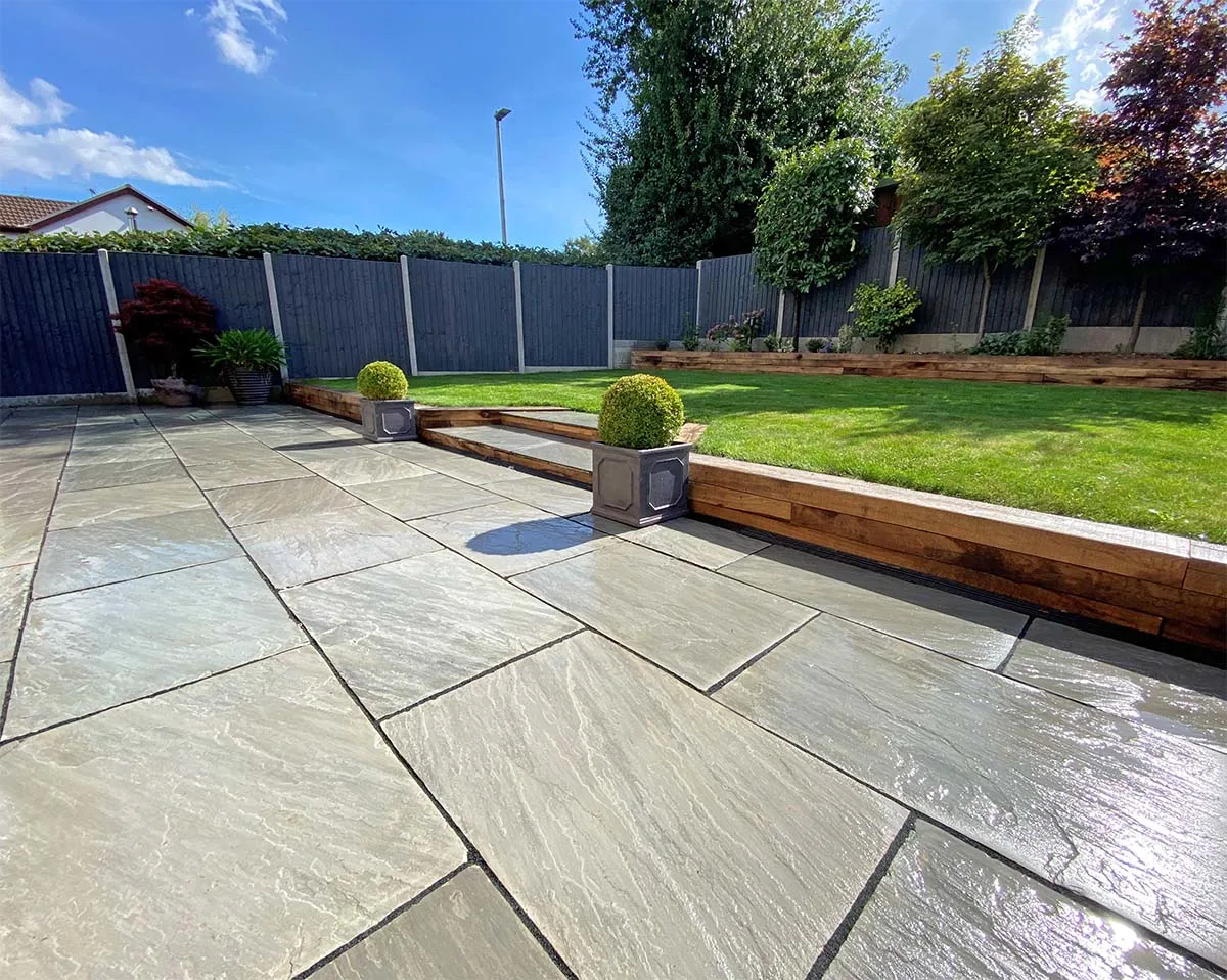 Grey sandstone patio with sleeper-edged raised lawn and topiary planters