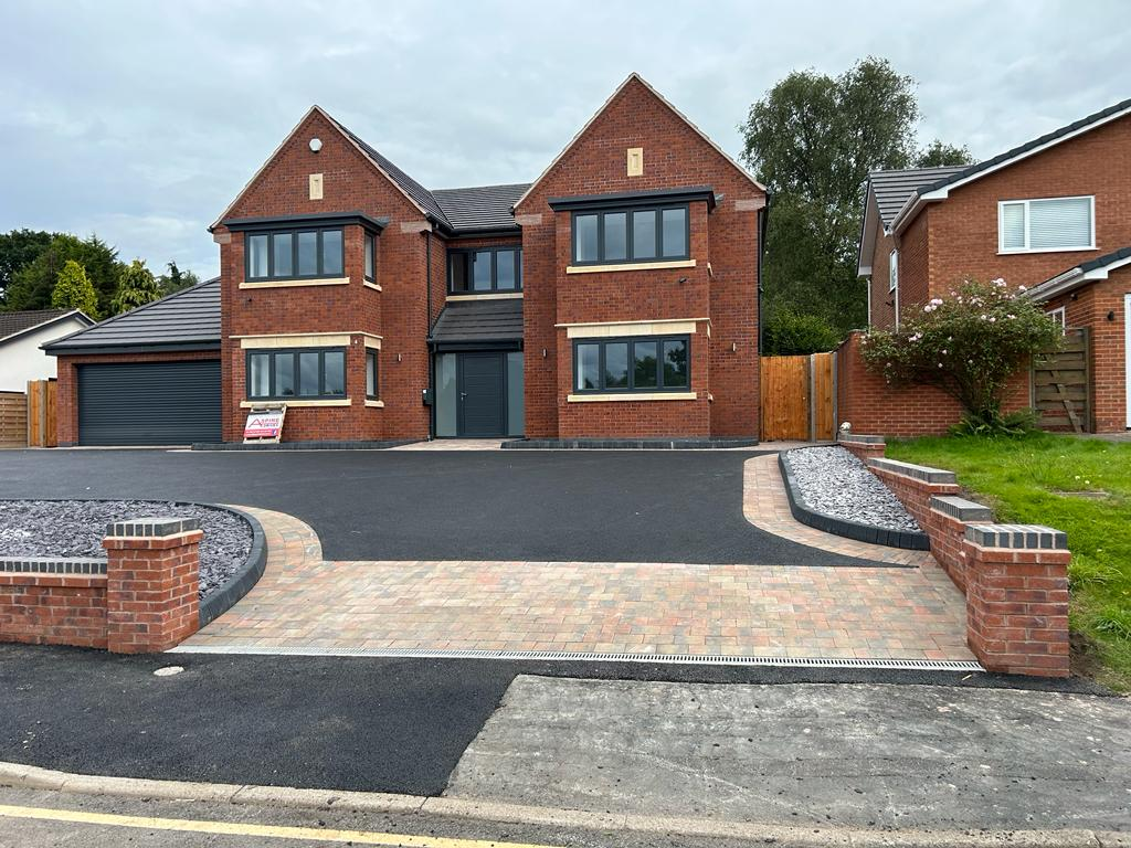 Wide tarmac driveway with brick pavers and retaining walls