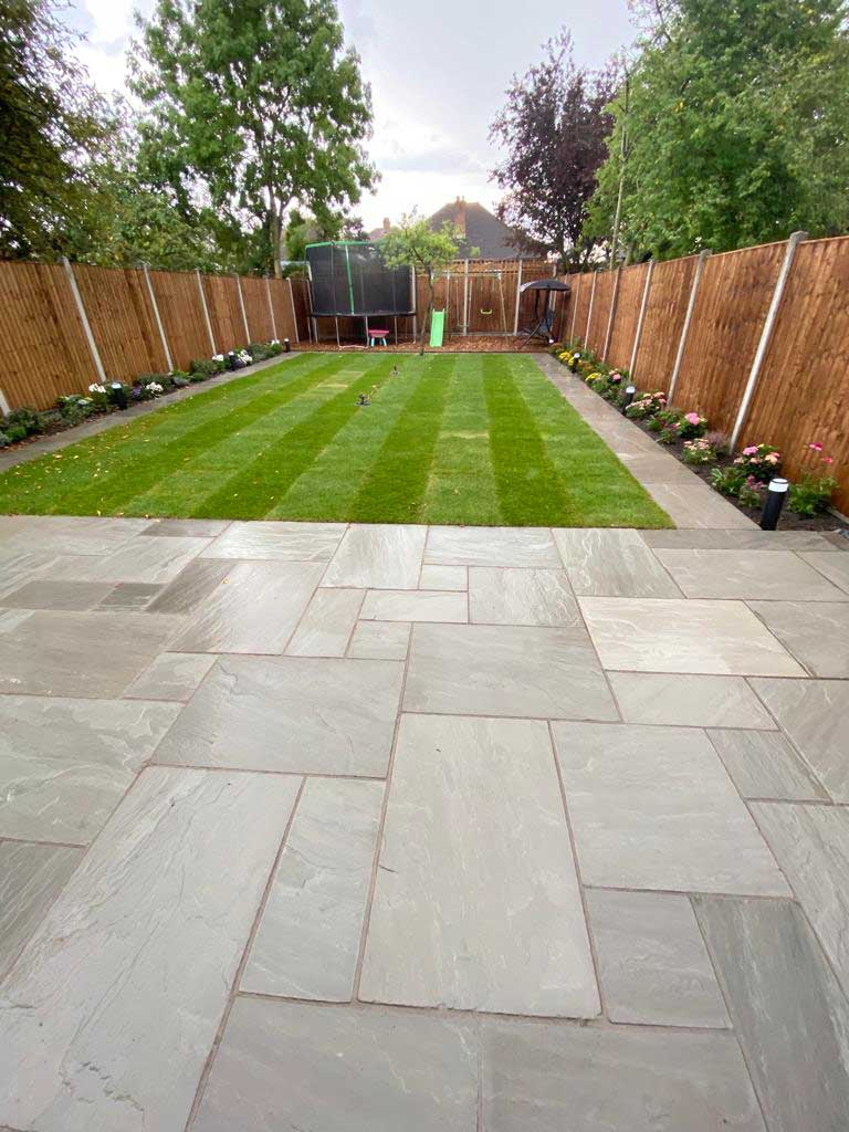 Grey sandstone patio leading to a striped lawn with planted borders